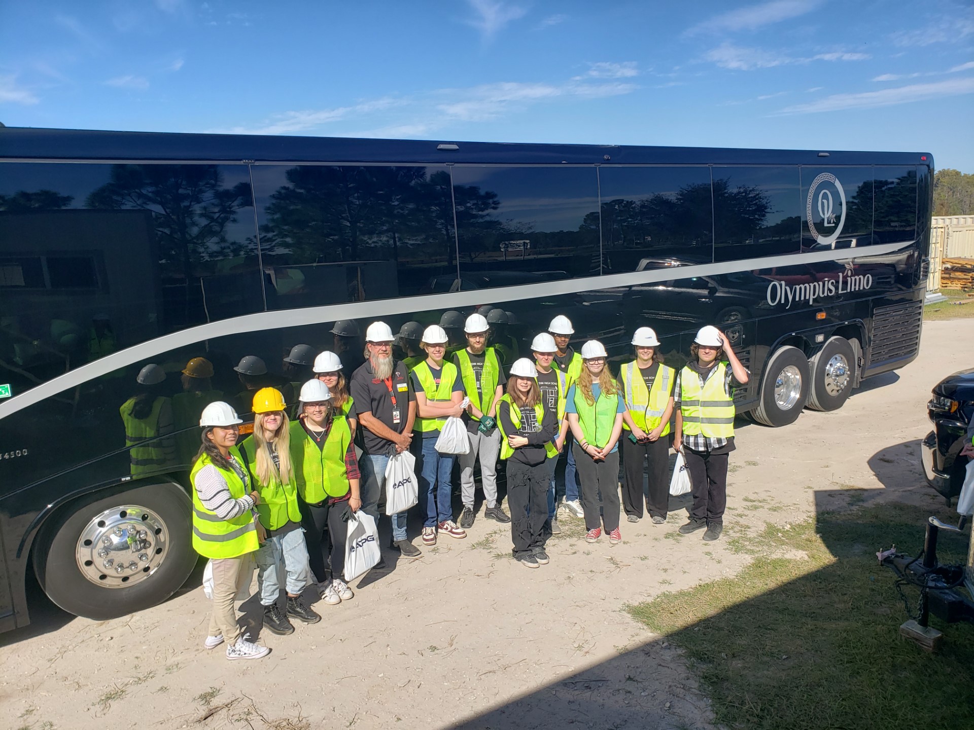 A group of people in hard hats and vests standing in front of a busDescription automatically generated